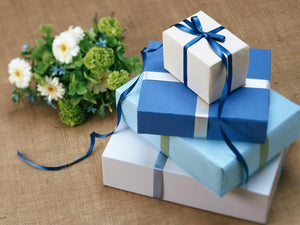 Four gift boxes stacked on top of each other with a small green & white bouquet. The cover image for the Gifts Collection.