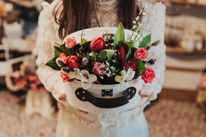 Woman holding a bouquet of tulips and other flowers partially enclosed in a small white suitcase