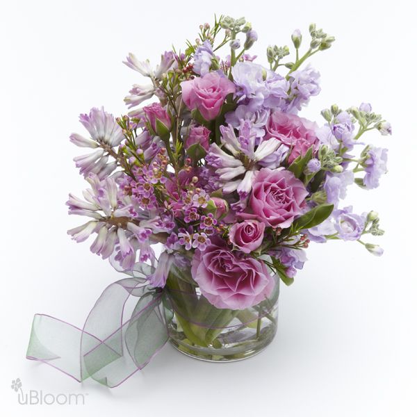 floral arrangement with spray stock flowers, spray roses, wax flowers, and hyacinth in a ribbon-wrapped clear vase