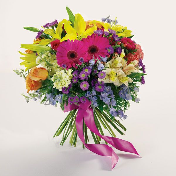 Floral arrangement of roses, lilies, delphinium, alstroemeria and more tied with a pink ribbon around the stems .