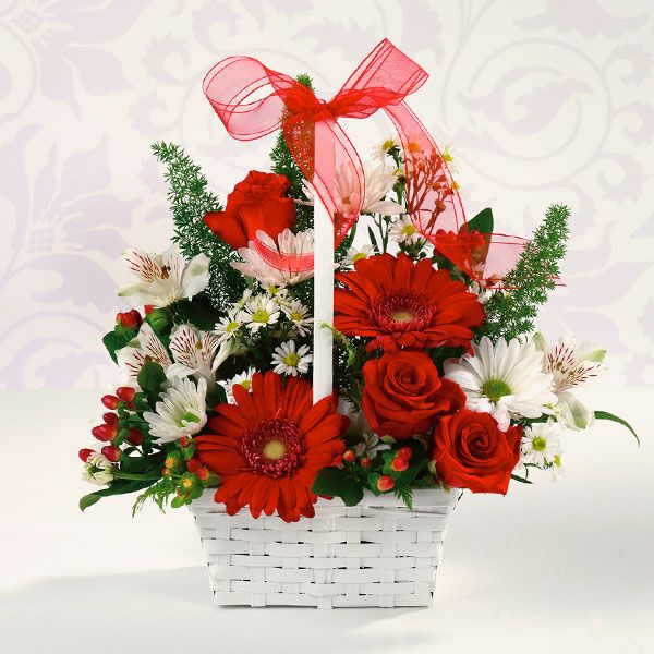 A floral arrangement in a white, weaved basket topped with a red ribbon and boasting fancy daisies, roses, alstroemeria and more.