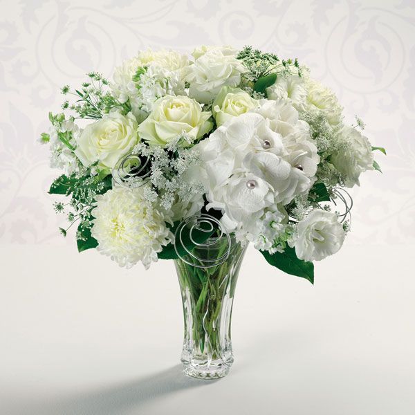 All white floral arrangement in a clear vase featuring pearl-studded hydrangea, white roses, Queen’s Anne’s lace, and football mums