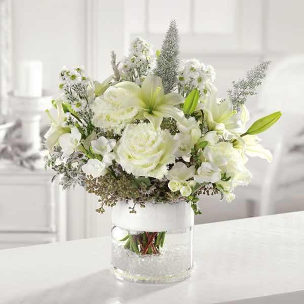 Holiday themed floral arrangement in a partially frosted vase featuring Asiatic lilies, roses, seeded eucalyptus and freesia.