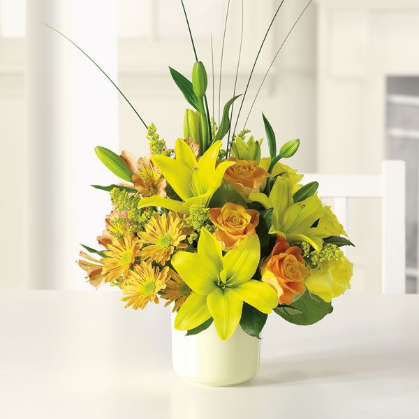 Floral arrangement in a white vase featuring bright yellow lilies and fire-orange roses