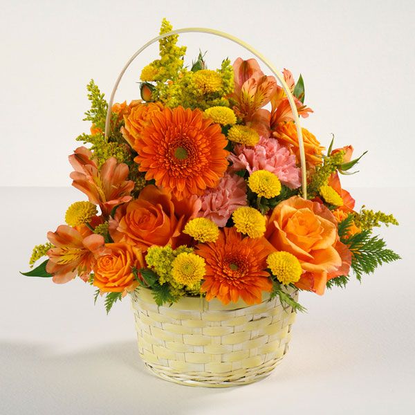 Vibrant and warm floral arrangement in a weaved basket featuring orange roses, alstroemeria, and more