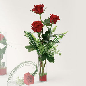 Floral arrangement in a glass vase featuring 3 red roses adorned by myrtle, eucalyptus, and Boston fern