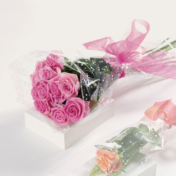 A bouquet of a dozen long-stemmed pink roses wrapped in clear plastic and tied with a sheer pink ribbon.