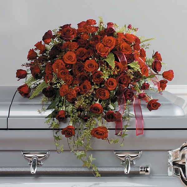 Prominent red rose casket floral arrangement featuring wine and candy red roses adorned with greenery.