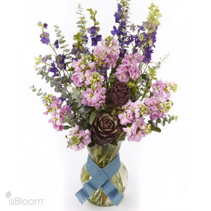 Ocean Side floral arrangement featuring larkspur, stock, artichoke, and eucalyptus in a clear glass vase with a blue ribbon.