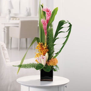 Elegant floral arrangement sitting in a black vase and featuring fresh ginger, protea and orchids.