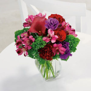 Floral arrangement in a clear glass vase featuring an elegant calla lily surrounded by roses, alstroemeria, carnations, and trachelium.